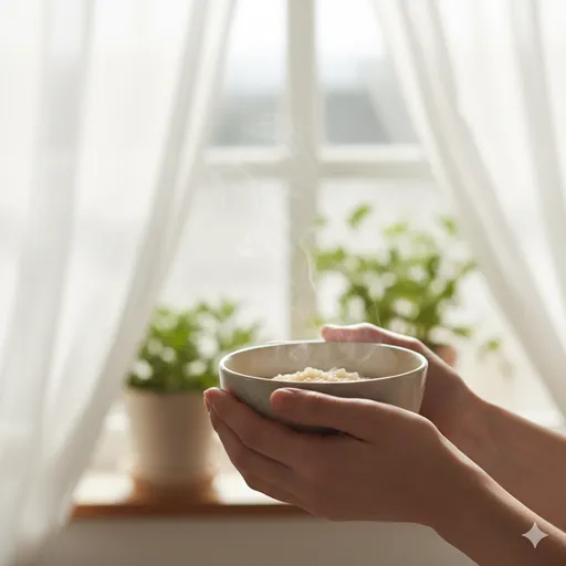湯気が立つお粥の茶碗を両手で包み込むように持ち、安らいでいるシーン。