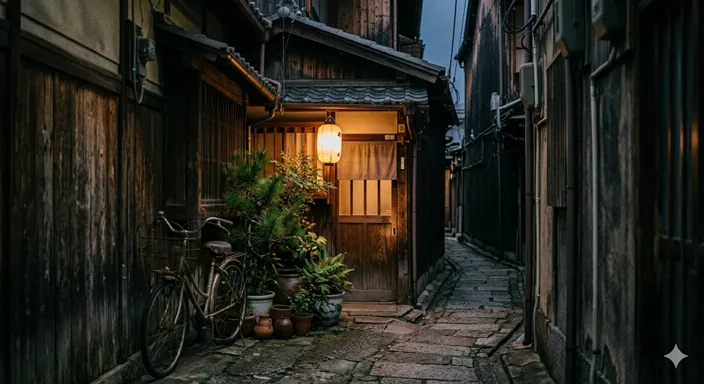 路地の奥に小さな灯りや植木、古い外壁が見え、生活感と隠れ家感が漂う路地裏の風景。